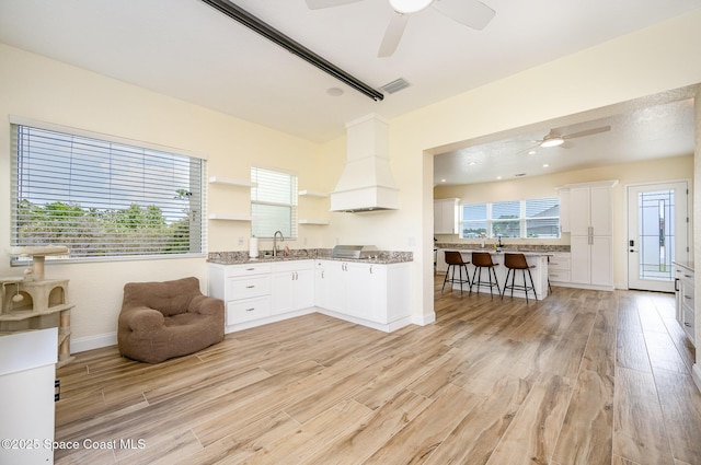 kitchen with premium range hood, visible vents, white cabinetry, open shelves, and light wood finished floors