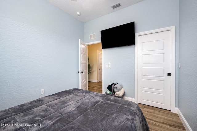 bedroom featuring a textured wall, wood finished floors, visible vents, and baseboards