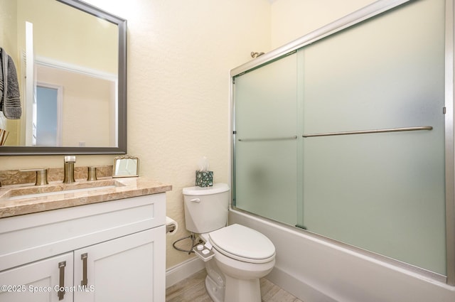 full bath with baseboards, combined bath / shower with glass door, vanity, and toilet