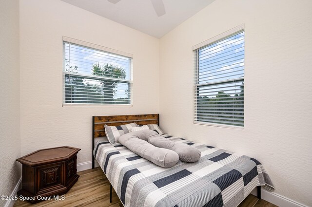 bedroom with a textured wall, wood finished floors, a ceiling fan, and baseboards