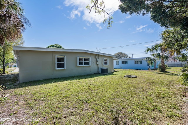 back of property with central air condition unit, a lawn, and stucco siding