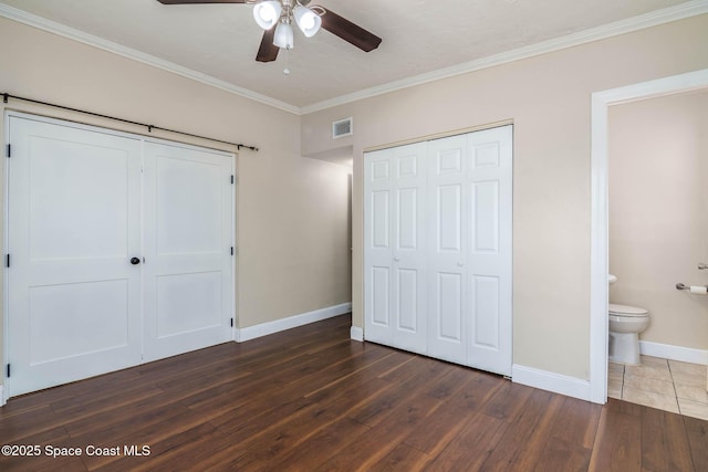 unfurnished bedroom with visible vents, wood finished floors, a barn door, crown molding, and baseboards