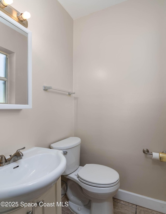 half bath with toilet, baseboards, and a sink