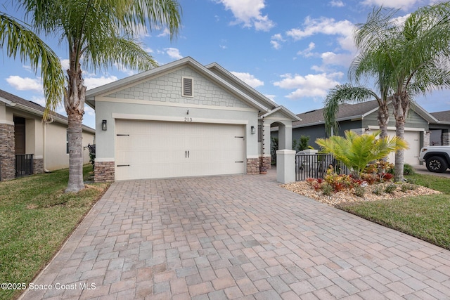 view of front of property with decorative driveway, stucco siding, a garage, stone siding, and a front lawn