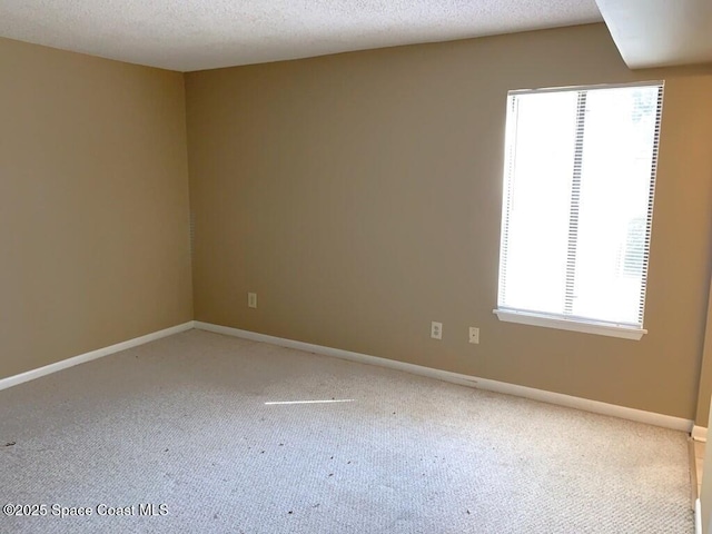 unfurnished room with light colored carpet, a healthy amount of sunlight, a textured ceiling, and baseboards