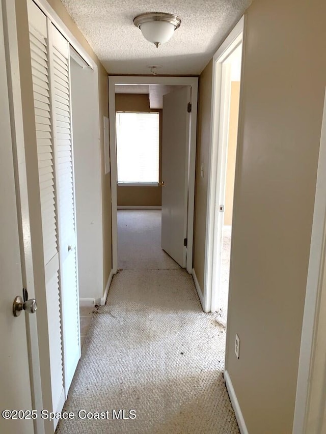 corridor with light carpet, baseboards, and a textured ceiling