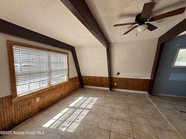 spare room with a wainscoted wall, a healthy amount of sunlight, a textured ceiling, and wooden walls