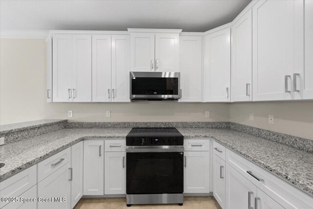 kitchen featuring light stone counters, white cabinets, stainless steel microwave, and electric range