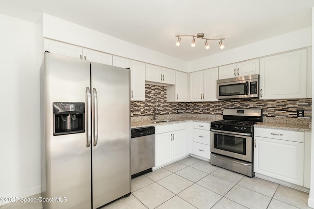 kitchen featuring light tile patterned floors, a sink, decorative backsplash, stainless steel appliances, and white cabinetry