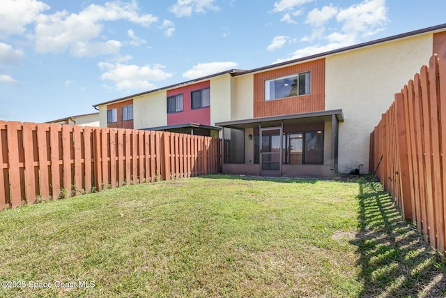 rear view of house featuring stucco siding, a yard, a fenced backyard, and a sunroom
