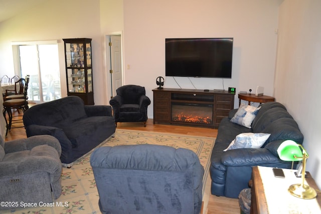 living area with wood finished floors, a glass covered fireplace, and vaulted ceiling