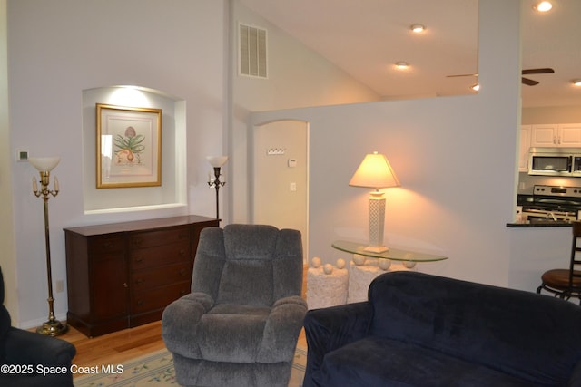 living area with visible vents, light wood-style floors, a ceiling fan, and vaulted ceiling