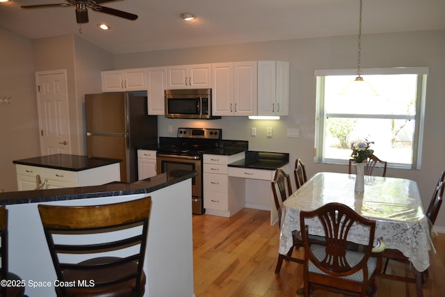 kitchen featuring a kitchen island, dark countertops, stainless steel appliances, white cabinets, and light wood finished floors