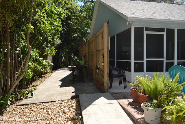 view of home's exterior featuring stucco siding, a patio, roof with shingles, and a sunroom