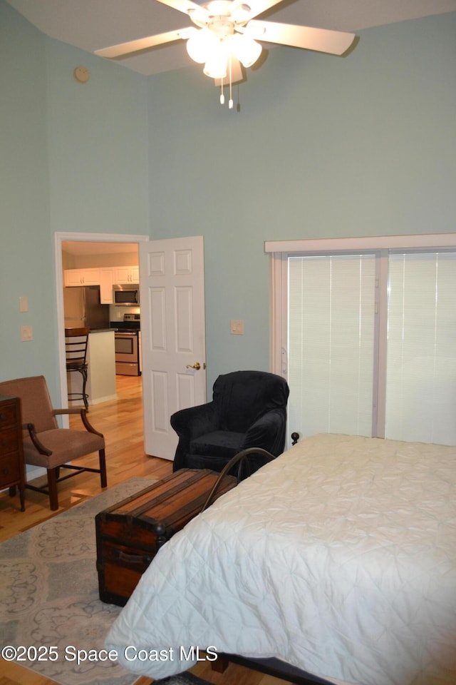 bedroom with light wood-style flooring, a ceiling fan, and a towering ceiling