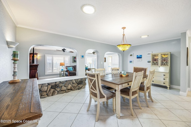 dining area with arched walkways, ceiling fan, light tile patterned flooring, and crown molding