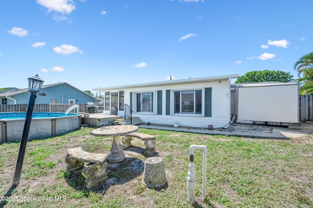 back of house with an outdoor structure, fence, a lawn, an outdoor pool, and a shed