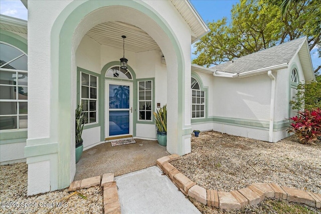 property entrance with stucco siding and a shingled roof