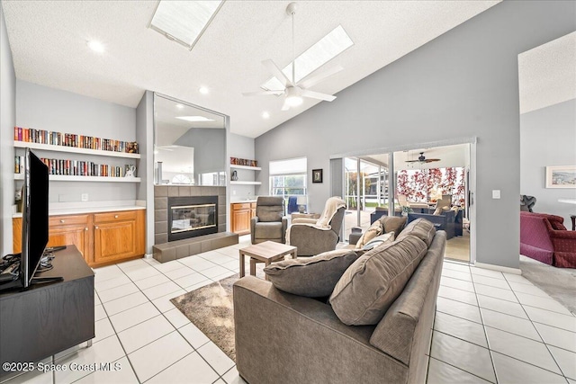 living room with light tile patterned floors, a tiled fireplace, high vaulted ceiling, and ceiling fan