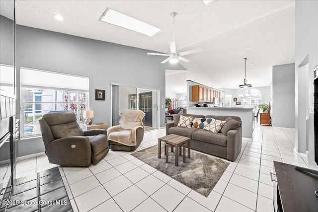 living area with high vaulted ceiling, a skylight, light tile patterned flooring, ceiling fan, and a textured ceiling