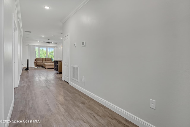 hall featuring baseboards, crown molding, visible vents, and wood finished floors