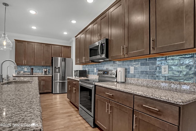 kitchen featuring decorative backsplash, light stone countertops, stainless steel appliances, crown molding, and a sink