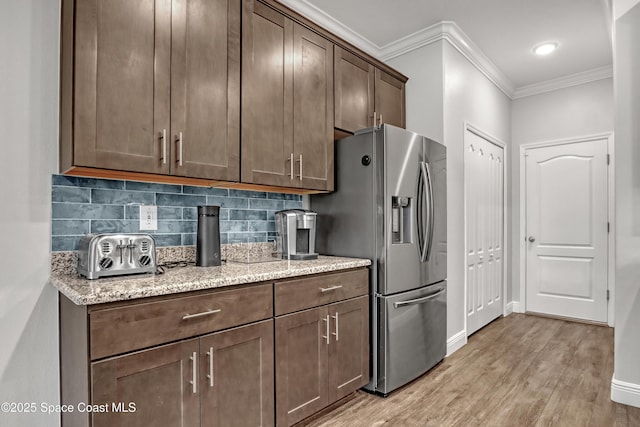 kitchen with light wood finished floors, tasteful backsplash, stainless steel fridge with ice dispenser, ornamental molding, and light stone counters