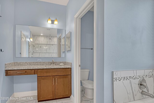 bathroom featuring marble finish floor, toilet, vanity, tiled shower, and baseboards