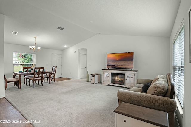 living room with lofted ceiling, light colored carpet, visible vents, an inviting chandelier, and a glass covered fireplace