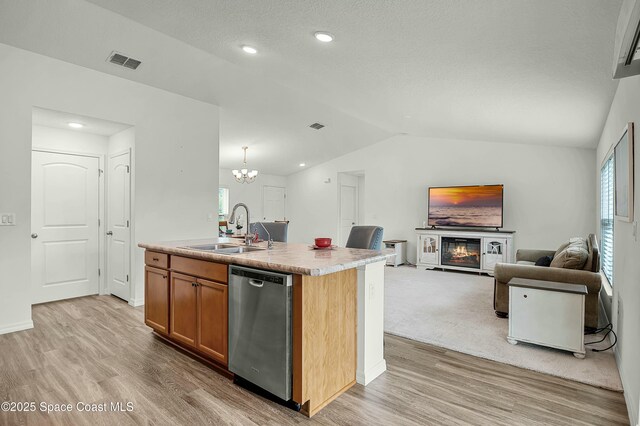 kitchen featuring visible vents, dishwasher, a glass covered fireplace, vaulted ceiling, and a sink