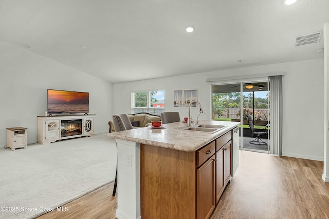 kitchen featuring visible vents, brown cabinetry, a glass covered fireplace, open floor plan, and a sink