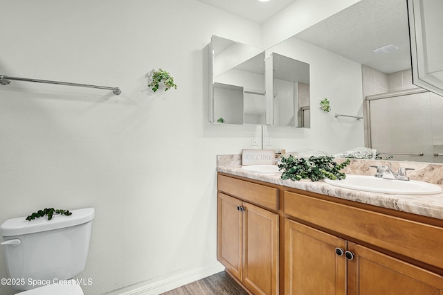 bathroom featuring double vanity, toilet, a sink, a shower stall, and wood finished floors