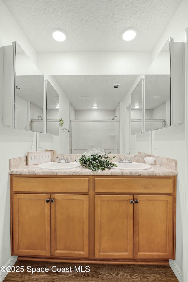 full bathroom with a textured ceiling, double vanity, a sink, and a shower stall