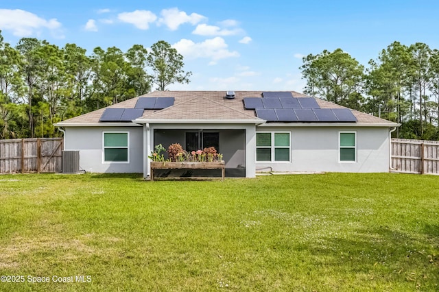 back of property with a lawn, a fenced backyard, central air condition unit, roof mounted solar panels, and stucco siding