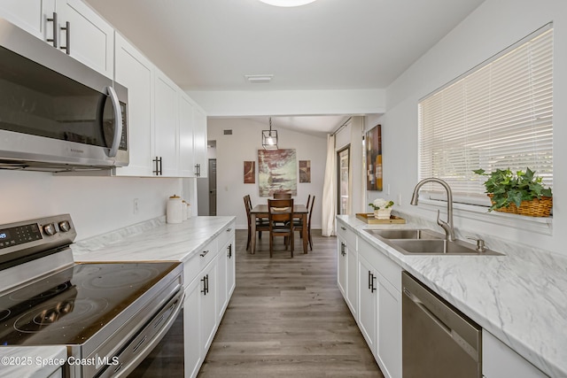 kitchen with appliances with stainless steel finishes, vaulted ceiling, white cabinetry, and a sink