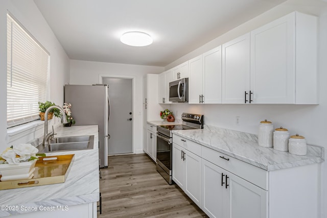 kitchen with stainless steel appliances, a sink, white cabinetry, and light wood-style floors