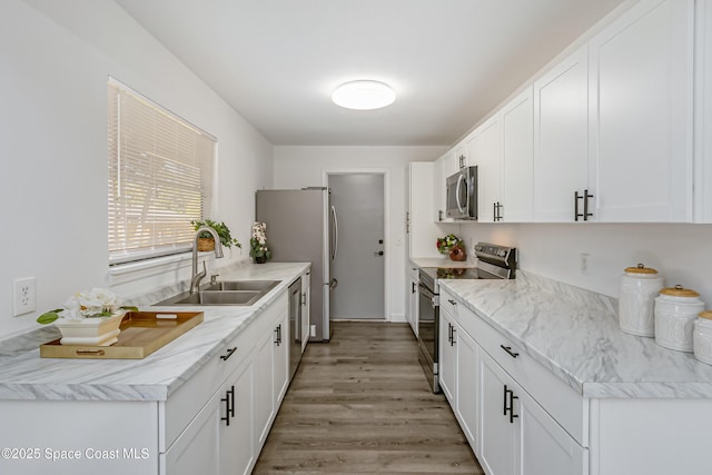 kitchen with appliances with stainless steel finishes, light wood-type flooring, a sink, and white cabinets