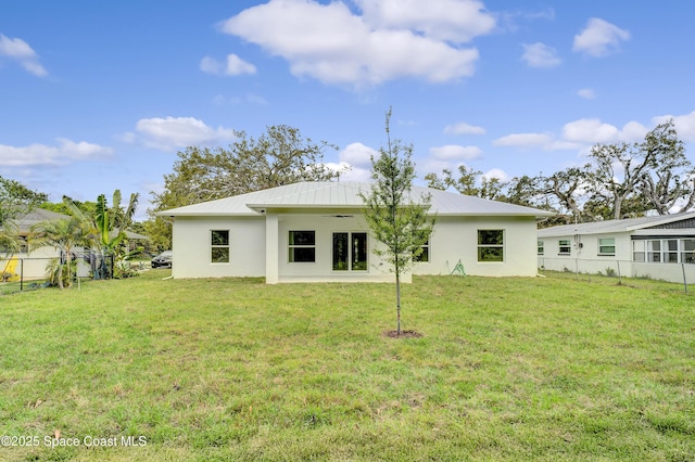 rear view of house with metal roof, a lawn, fence, and stucco siding