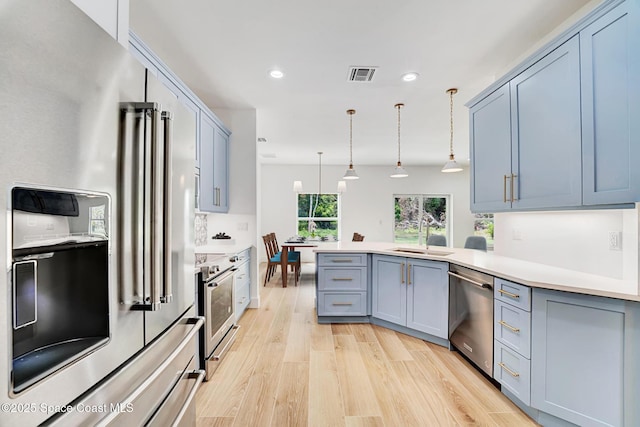 kitchen featuring light wood finished floors, stainless steel appliances, visible vents, a sink, and a peninsula