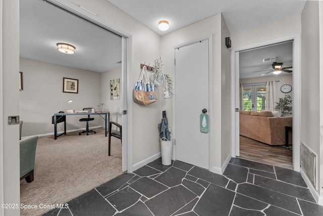 entrance foyer with a textured ceiling, dark carpet, visible vents, and baseboards