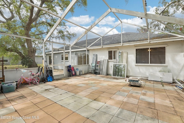 rear view of house with a patio area, roof with shingles, glass enclosure, and stucco siding