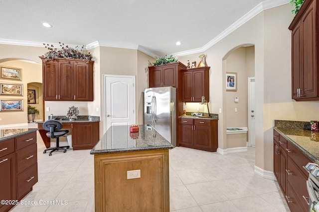 kitchen featuring arched walkways, stainless steel fridge, dark stone counters, and ornamental molding