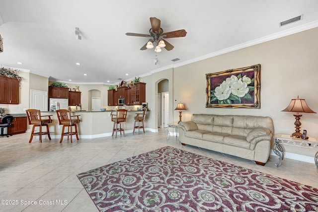 living area featuring light tile patterned floors, visible vents, arched walkways, ornamental molding, and ceiling fan