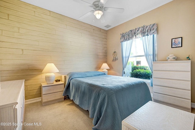 bedroom featuring light carpet, wood walls, and a ceiling fan