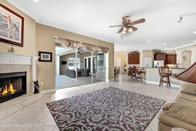 living area with crown molding, light tile patterned floors, arched walkways, and ceiling fan