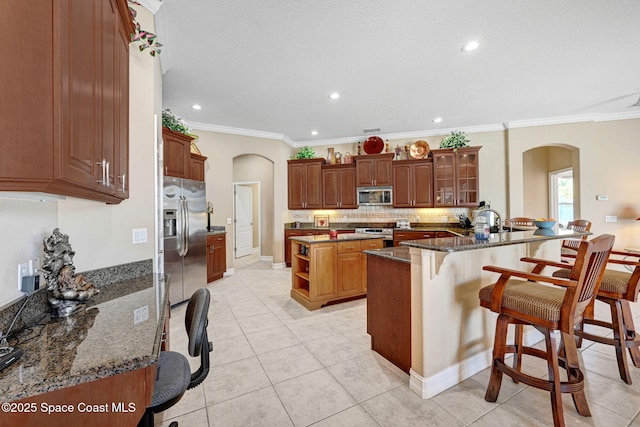 kitchen with arched walkways, a kitchen island, a kitchen breakfast bar, and stainless steel appliances