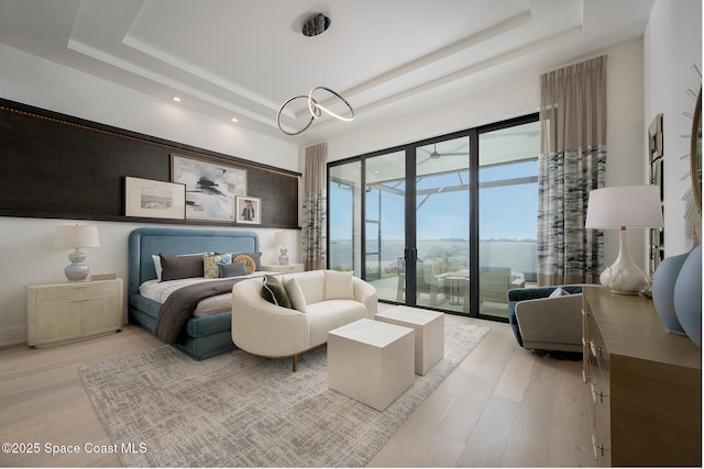 bedroom with light wood-style floors, a tray ceiling, access to exterior, and french doors