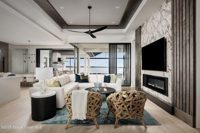 living room with ceiling fan, a fireplace, a tray ceiling, and wood finished floors