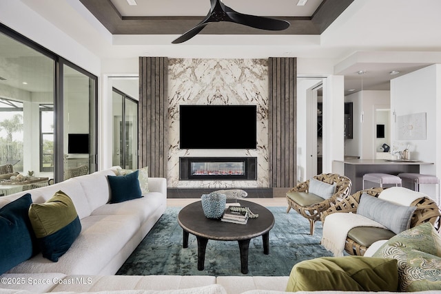 living room featuring ceiling fan, a fireplace, and a tray ceiling