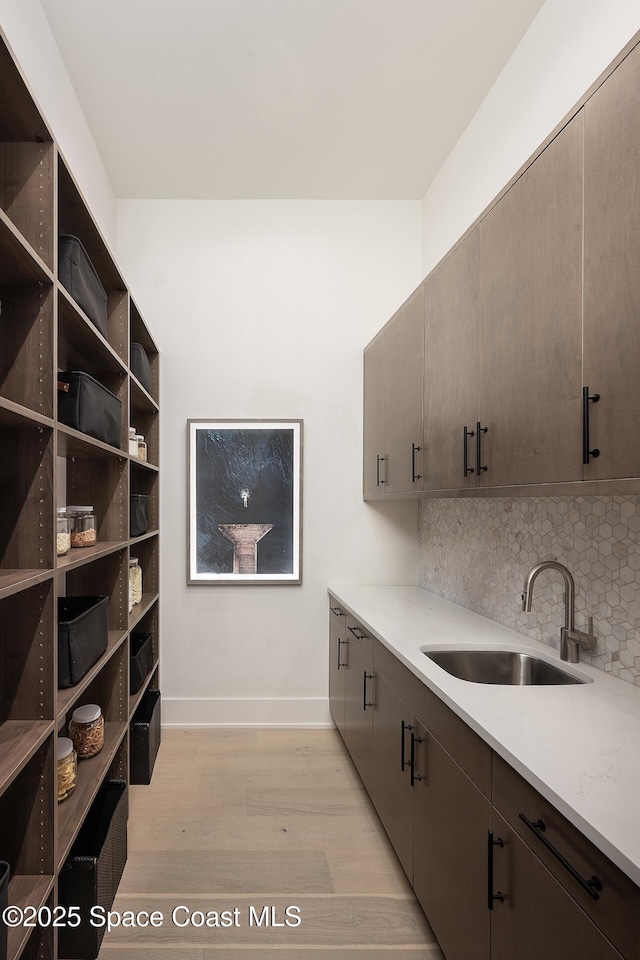 kitchen with dark brown cabinetry, light wood finished floors, tasteful backsplash, light countertops, and a sink